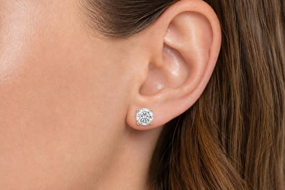 Close-up side view of a model wearing yellow metal stud earrings with round white gemstones in a four-prong setting.