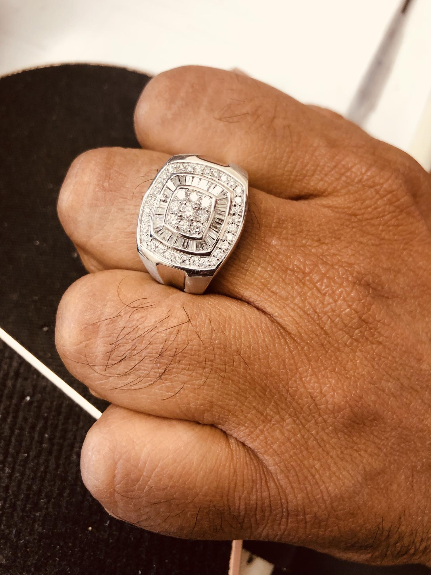 White metal ring with a square face featuring a large central cluster of round white gemstones, surrounded by a border of baguette and round white gemstones, shown worn on a hand in a model, angled from above.
