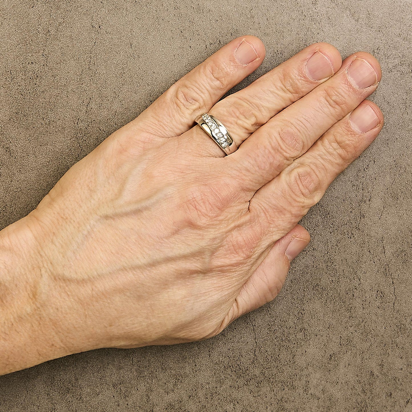 White metal ring with a channel setting of round white gemstones, shown worn on a model's hand from a top angle.
