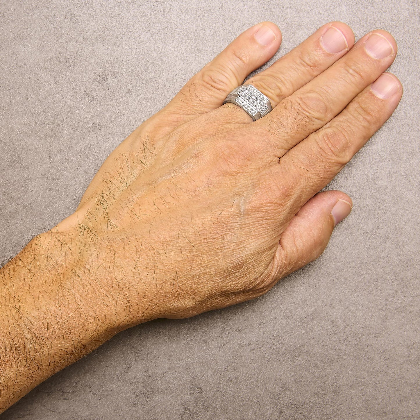 White metal ring with multiple round white gemstones in prong settings, shown worn on a model's hand from a top-down angle.
