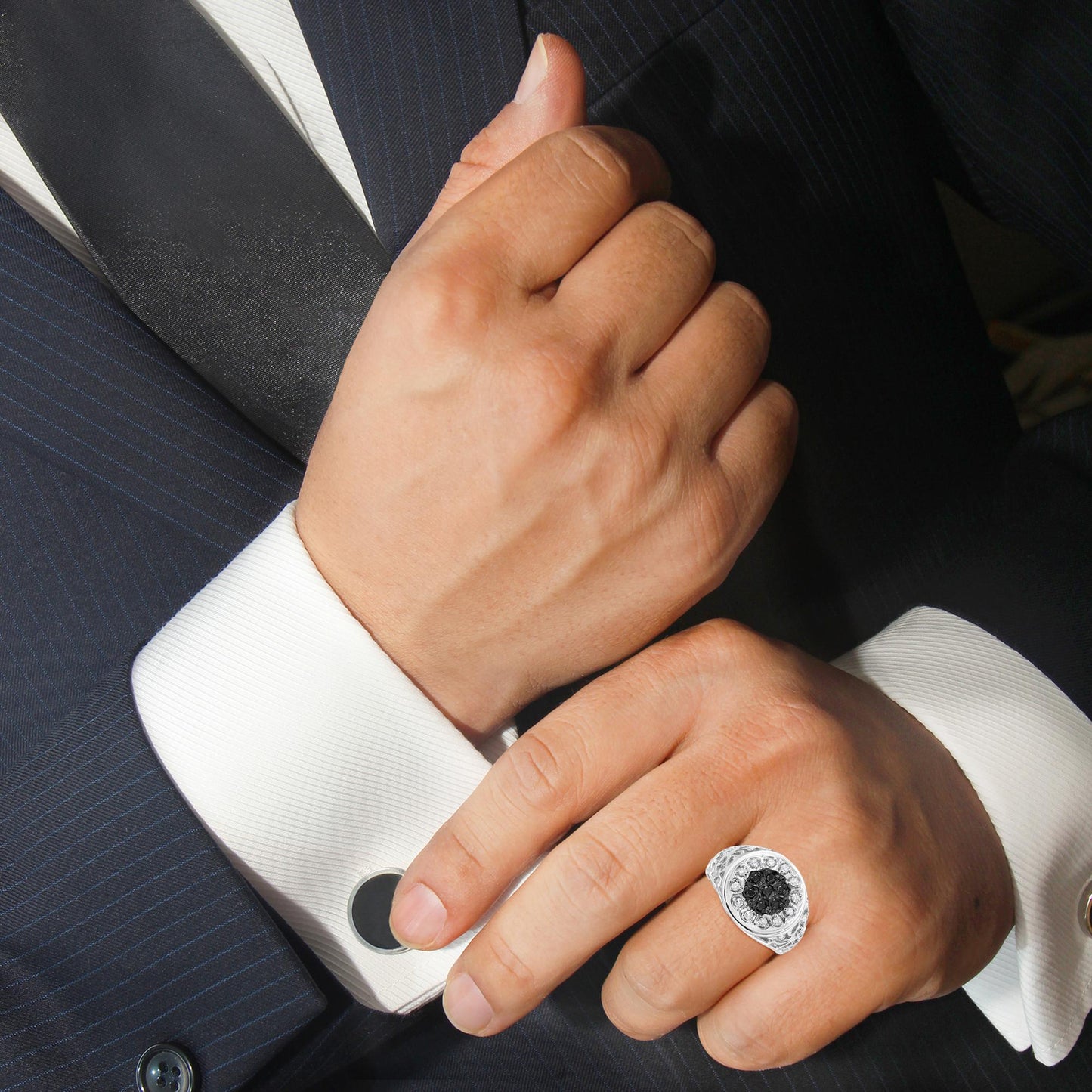 Close-up of a white metal ring with round black and white gemstones in prong settings, worn on a model’s finger, shot from an angled top view.
