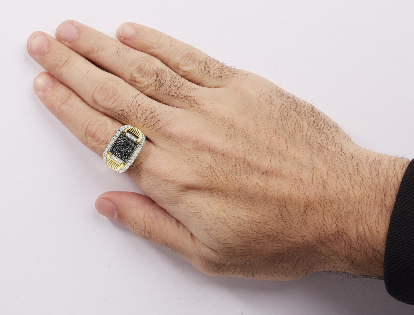 Yellow metal ring with a rectangular top featuring a cluster of black gemstones surrounded by two rows of white gemstones, worn on a model's hand, shot from above at an angle.