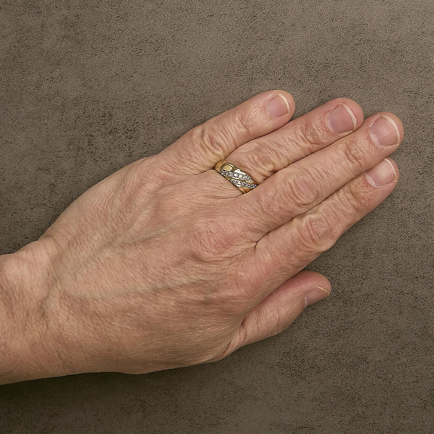 Yellow ring with intertwined bands featuring white round gemstones in prong settings, worn on a model's finger, shown from a top angle.