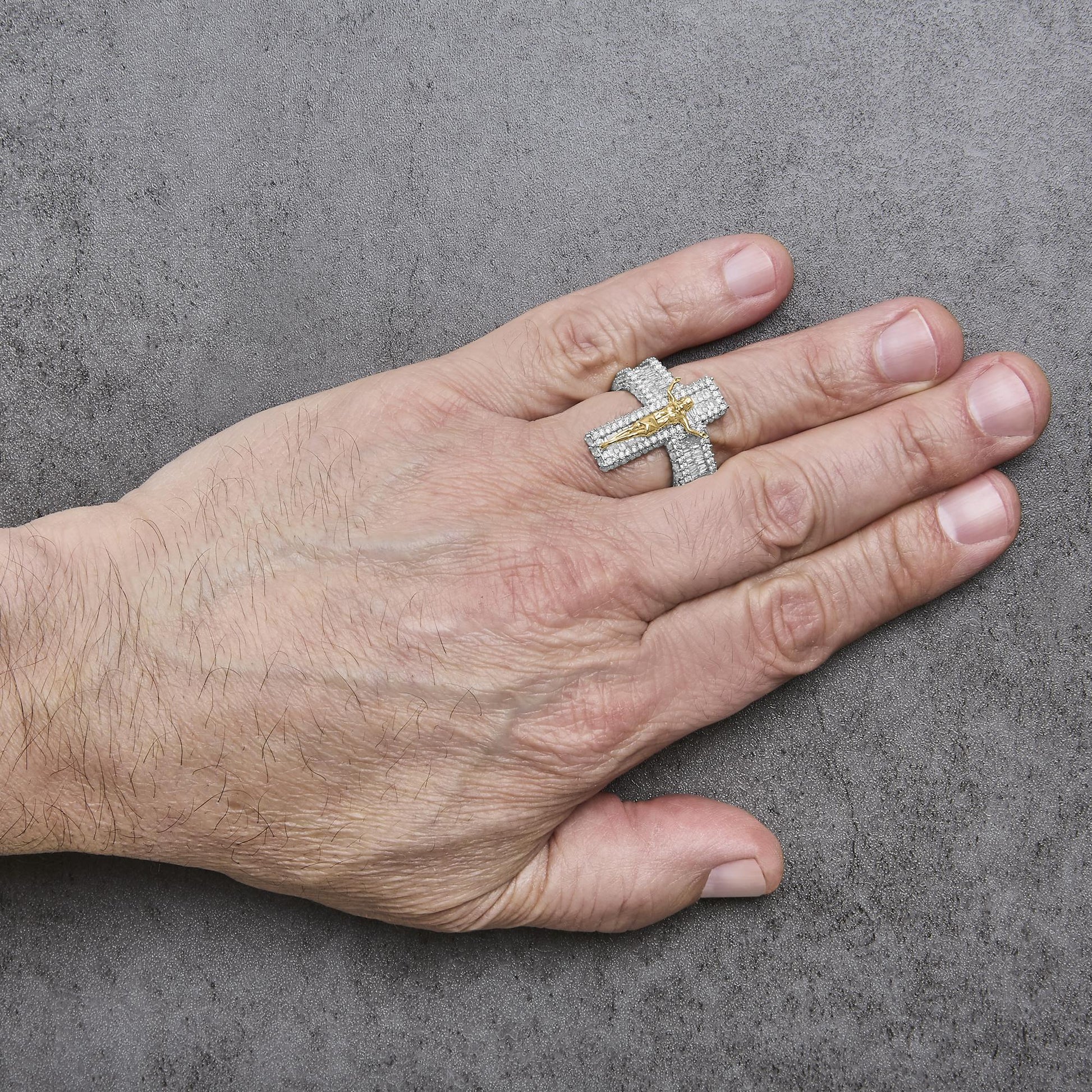 Close-up angled view of a model's hand wearing a yellow ring designed as a cross with white round and baguette gemstones in prong settings, featuring a small yellow figure in the center.