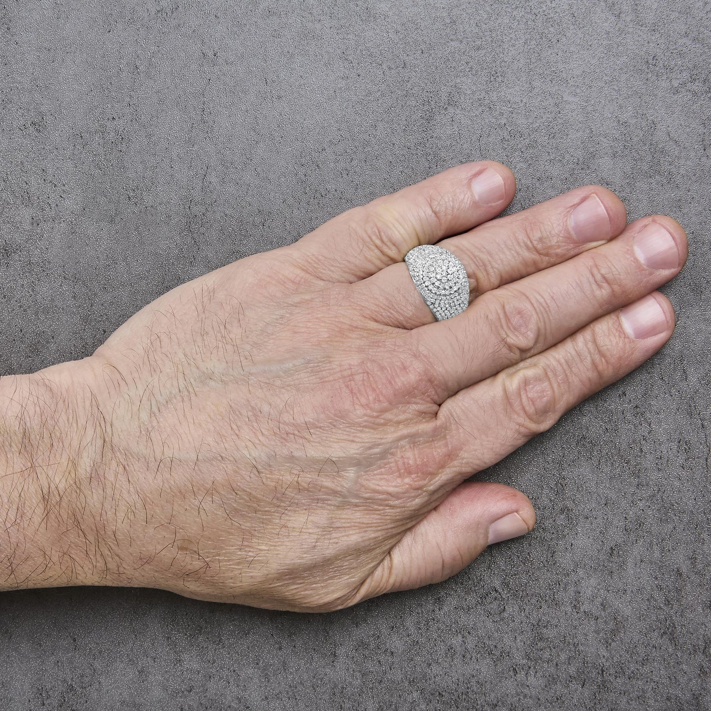 Yellow metal ring with round white gemstones in prong setting covering the top, shown worn on a model's finger from a top angle on a gray textured background.