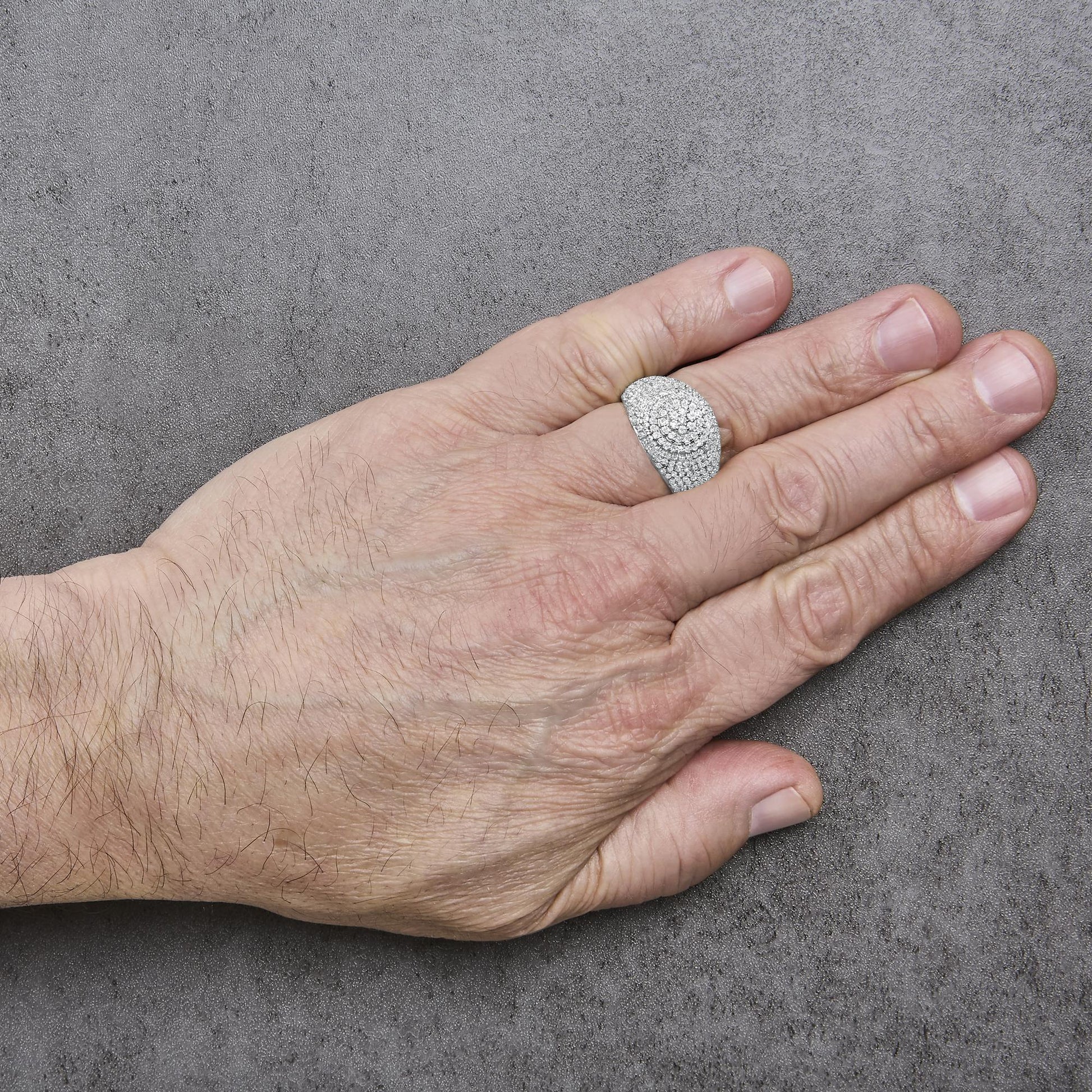 Yellow metal ring with round white gemstones in prong setting covering the top, shown worn on a model's finger from a top angle on a gray textured background.