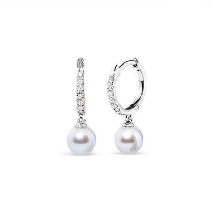 Pair of white metal hoop earrings with small white gemstones in pave setting along the front, each featuring a round white dangling gemstone, shown in a front and angled side view on a white background.