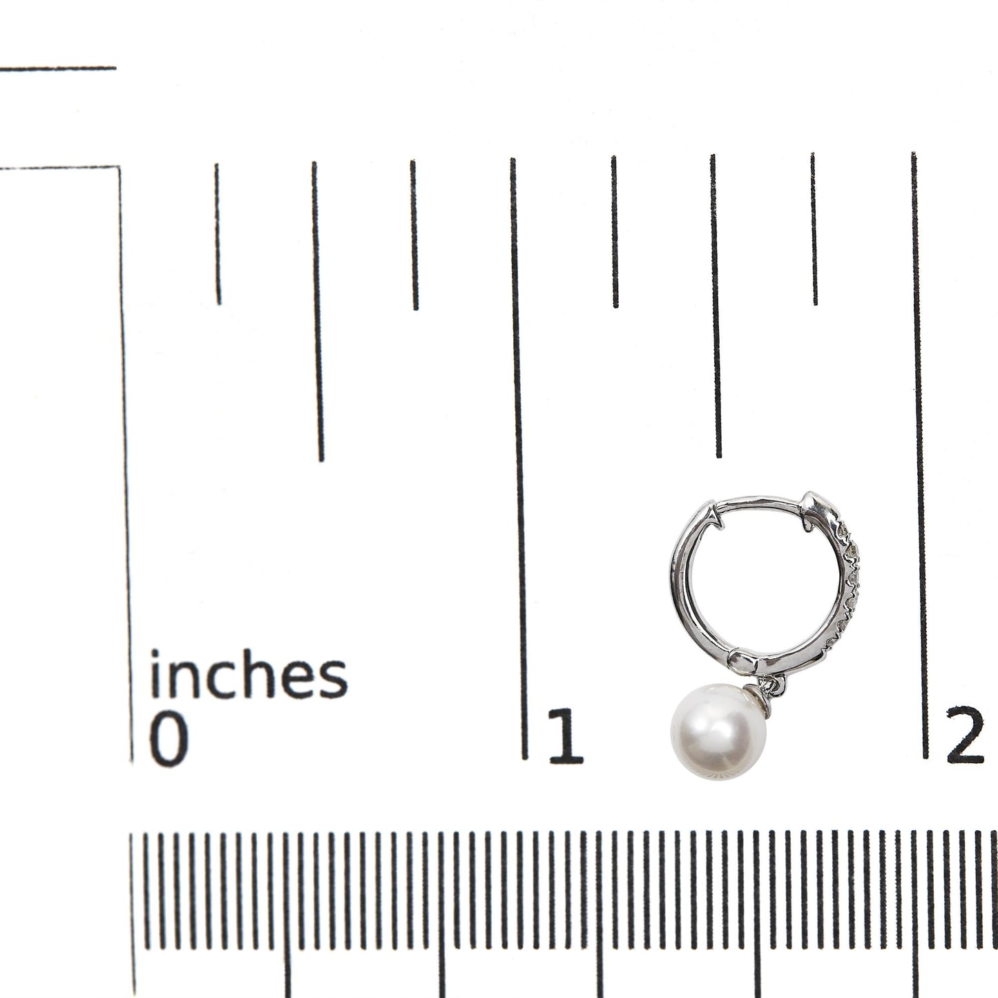 White metal hoop earring with pave-set white gemstones and a single round white pearl dangle, shown on a ruler for size reference, front angle.