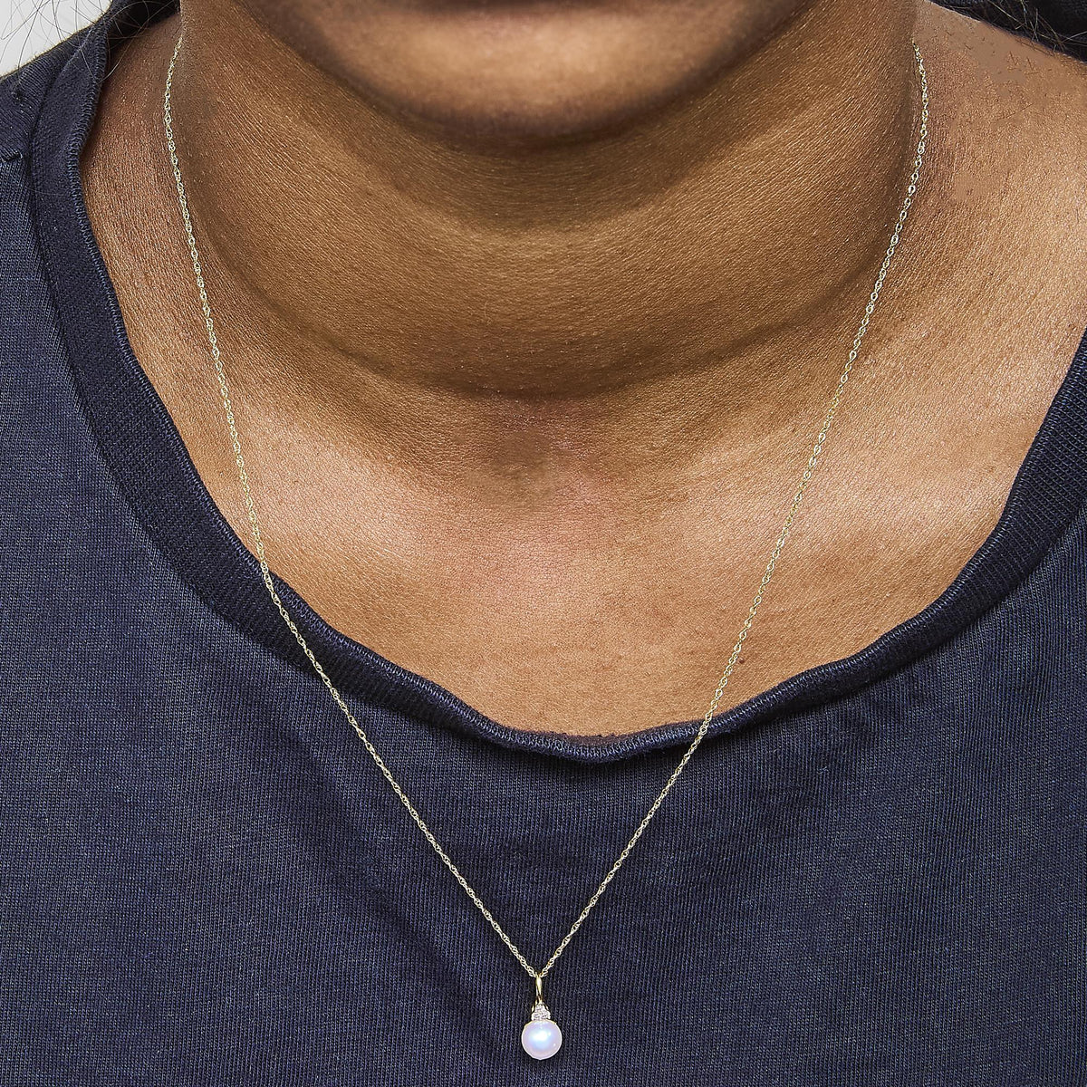 Close-up front view of a model wearing a yellow metal necklace with a round pendant featuring a white gemstone and three small white gemstones in prong settings above it.