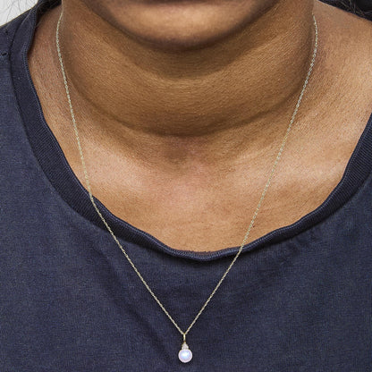Close-up front view of a model wearing a yellow metal necklace with a round pendant featuring a white gemstone and three small white gemstones in prong settings above it.