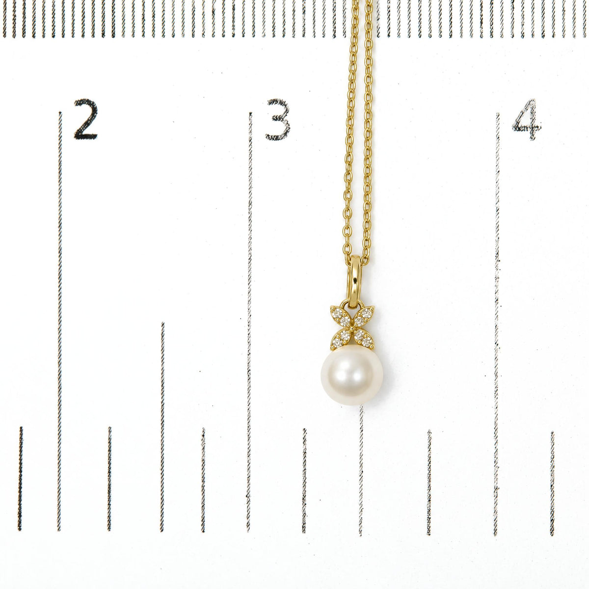 Close-up front view of a yellow metal necklace shown on a scale, featuring a pendant with a round white gemstone and a floral design with small white gemstones in prong settings.