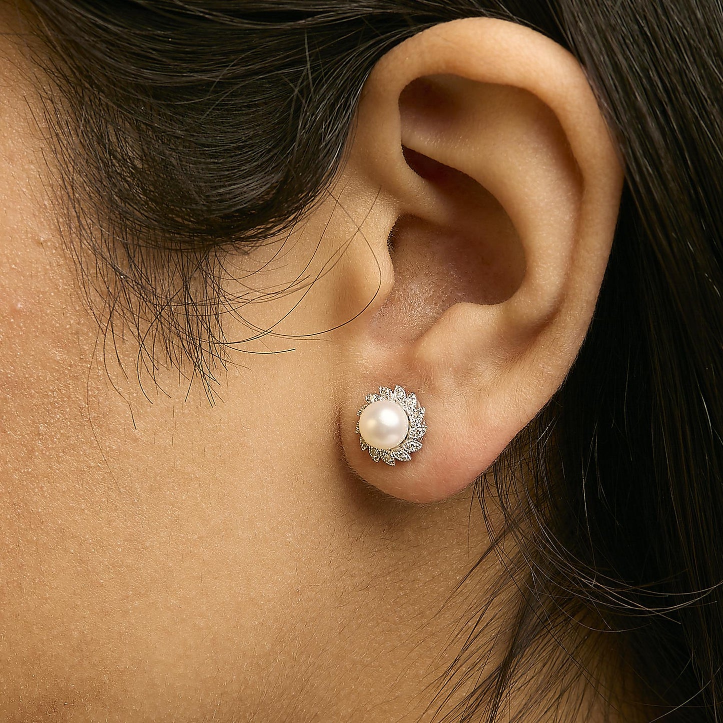 Close-up side view of a model wearing a white metal stud earring featuring a central round white gemstone surrounded by smaller white gemstones in a pave setting.