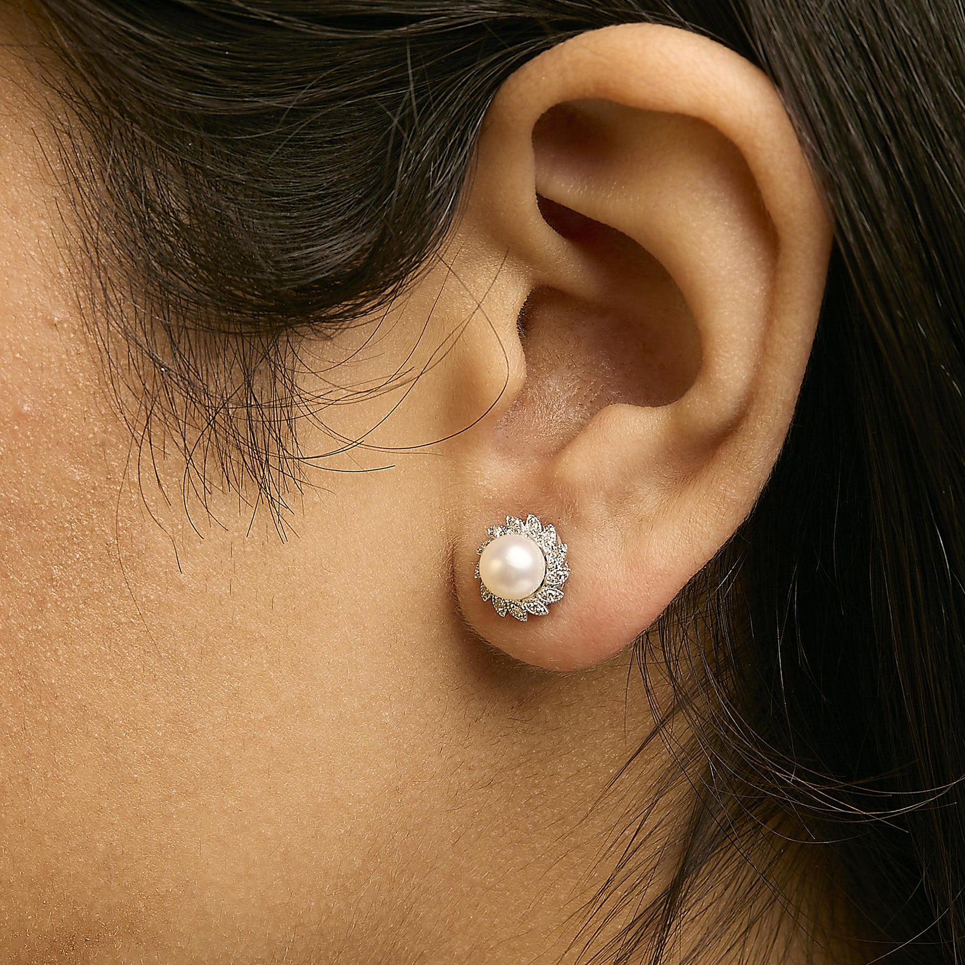 Close-up side view of a model wearing a white metal stud earring featuring a central round white gemstone surrounded by smaller white gemstones in a pave setting.