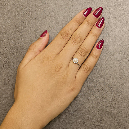 White metal ring with a central round white gemstone surrounded by a halo of small white gemstones, shown worn on a model's hand from a top-down angle.