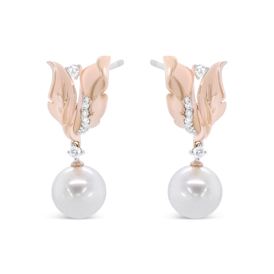 Front view of rose-colored metal earrings designed as leaves with white round gemstones in prong settings and large white round pearls hanging below.