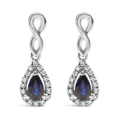 Front view of white metal infinity-shaped drop earrings with pear-shaped blue gemstones surrounded by a halo of small round white gemstones.