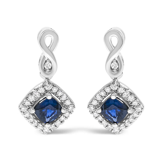 Front view of a pair of white metal earrings featuring an infinity loop at the top with a small white gemstone in the center, and a cushion-shaped blue gemstone surrounded by a border of round white gemstones in a prong setting.