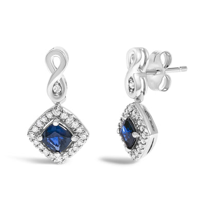 Front and side view of white metal earrings with an infinity-shaped top and a square-shaped drop featuring a blue gemstone center surrounded by small white gemstones.
