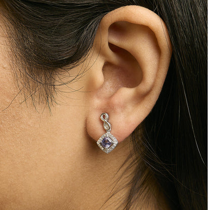 Close-up side view of a model wearing white metal earrings featuring a blue cushion-shaped gemstone surrounded by small white round gemstones, with an infinity loop detail at the top.