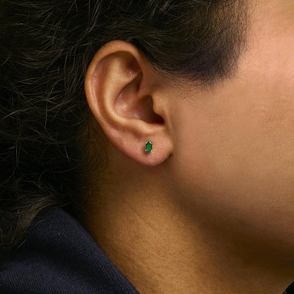 Close-up side view of a yellow metal stud earring with an oval green gemstone in a prong setting, worn on a model's ear.