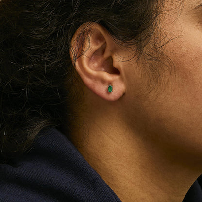 Close-up side view of a model wearing white metal stud earrings featuring oval green gemstones in prong settings.