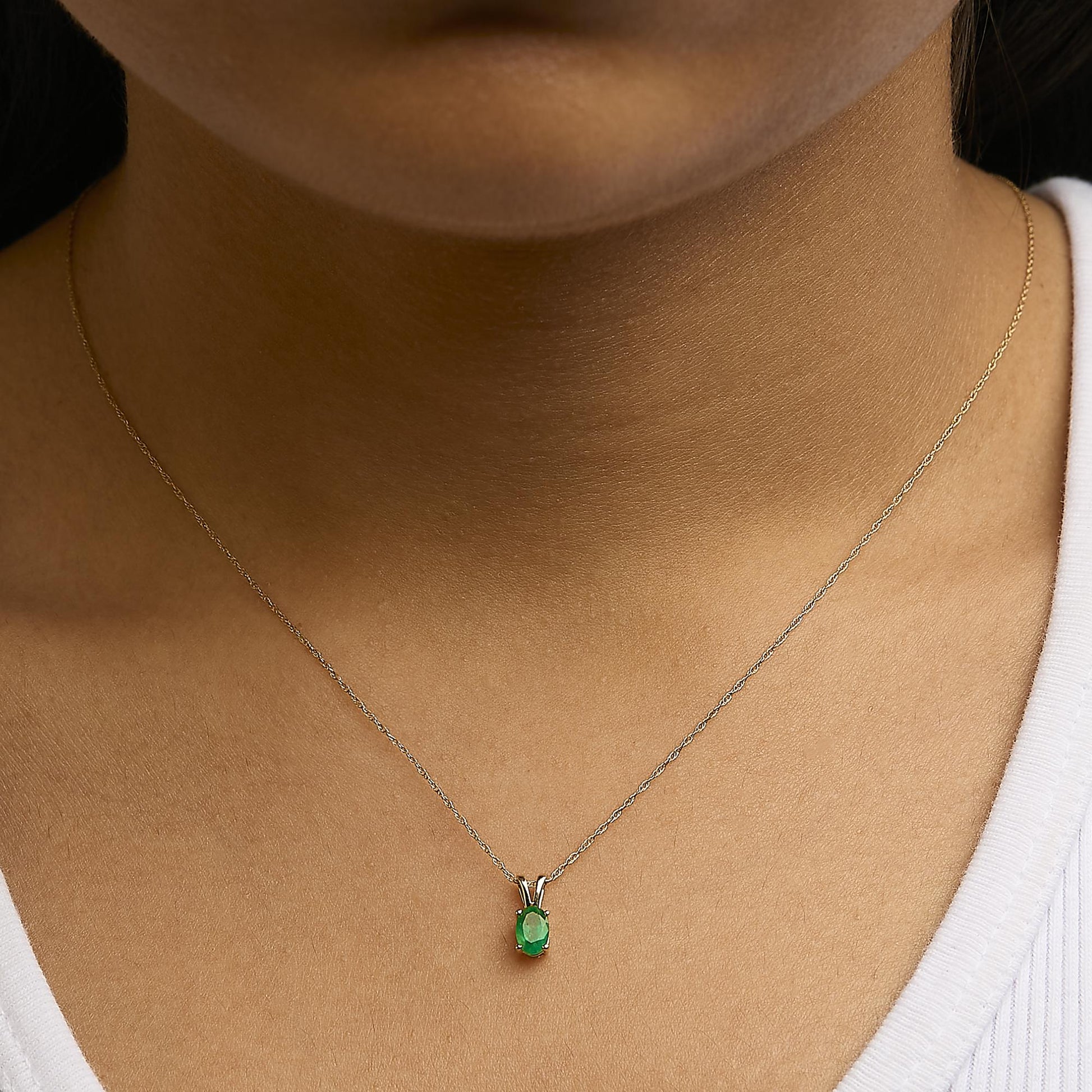 Yellow metal necklace with an oval green gemstone set in a 4-prong setting, worn on a model shown from a front close-up angle.