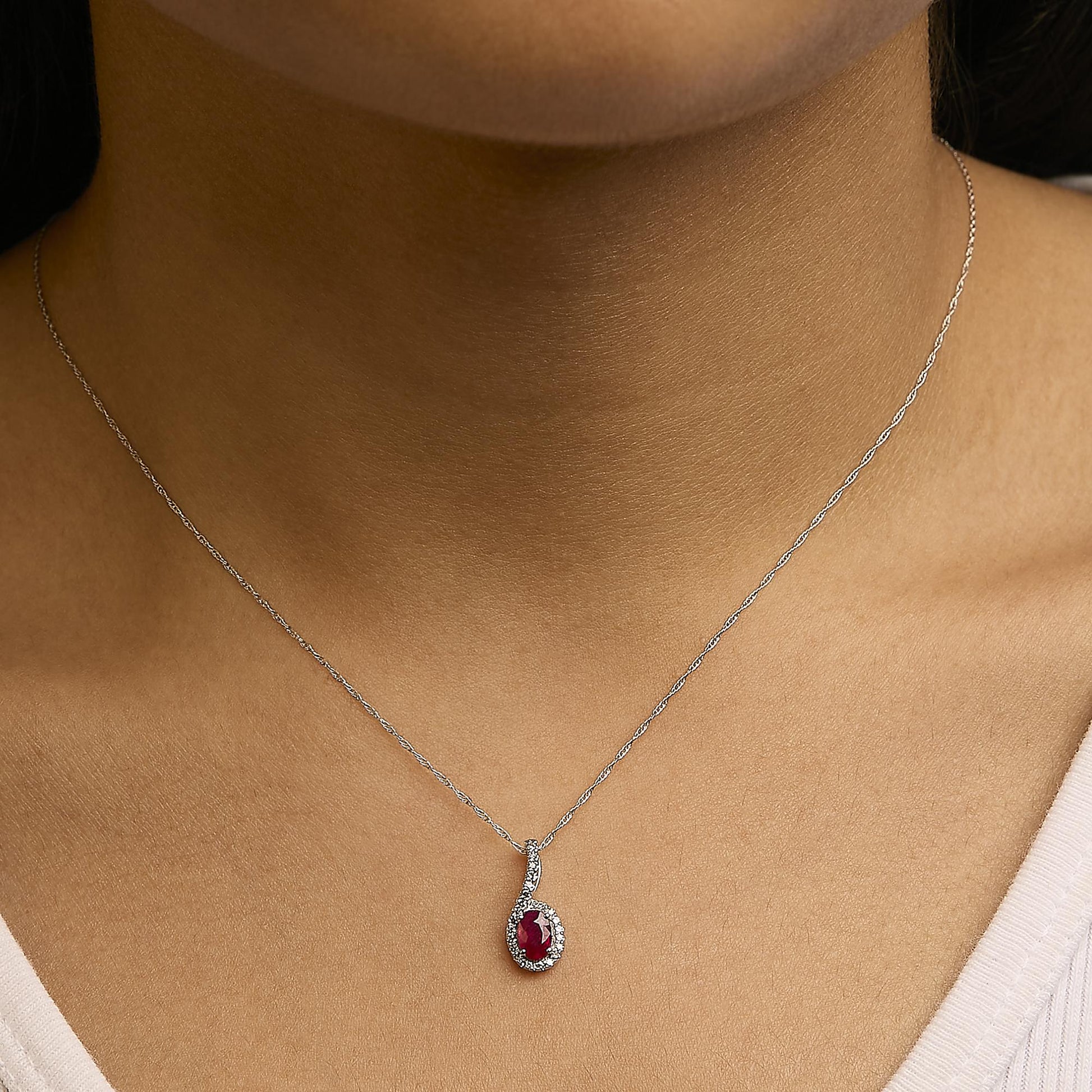 Close-up front view of a necklace with a white metal chain, featuring a pendant with one oval red gemstone surrounded by small round white gemstones, shown worn on a model.
