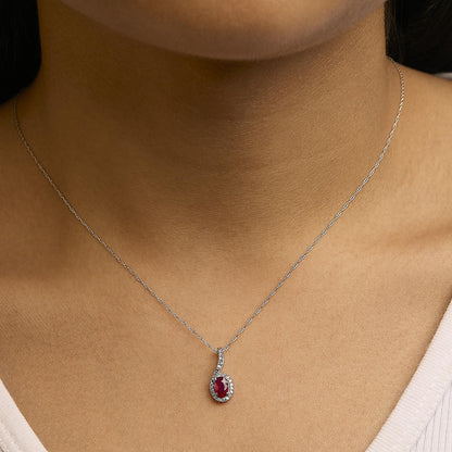 Close-up front view of a necklace with a white metal chain, featuring a pendant with one oval red gemstone surrounded by small round white gemstones, shown worn on a model.