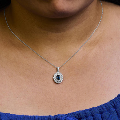 White necklace with oval-shaped blue gemstone surrounded by round white gemstones in prong setting, shown worn on a model, front close-up angle.