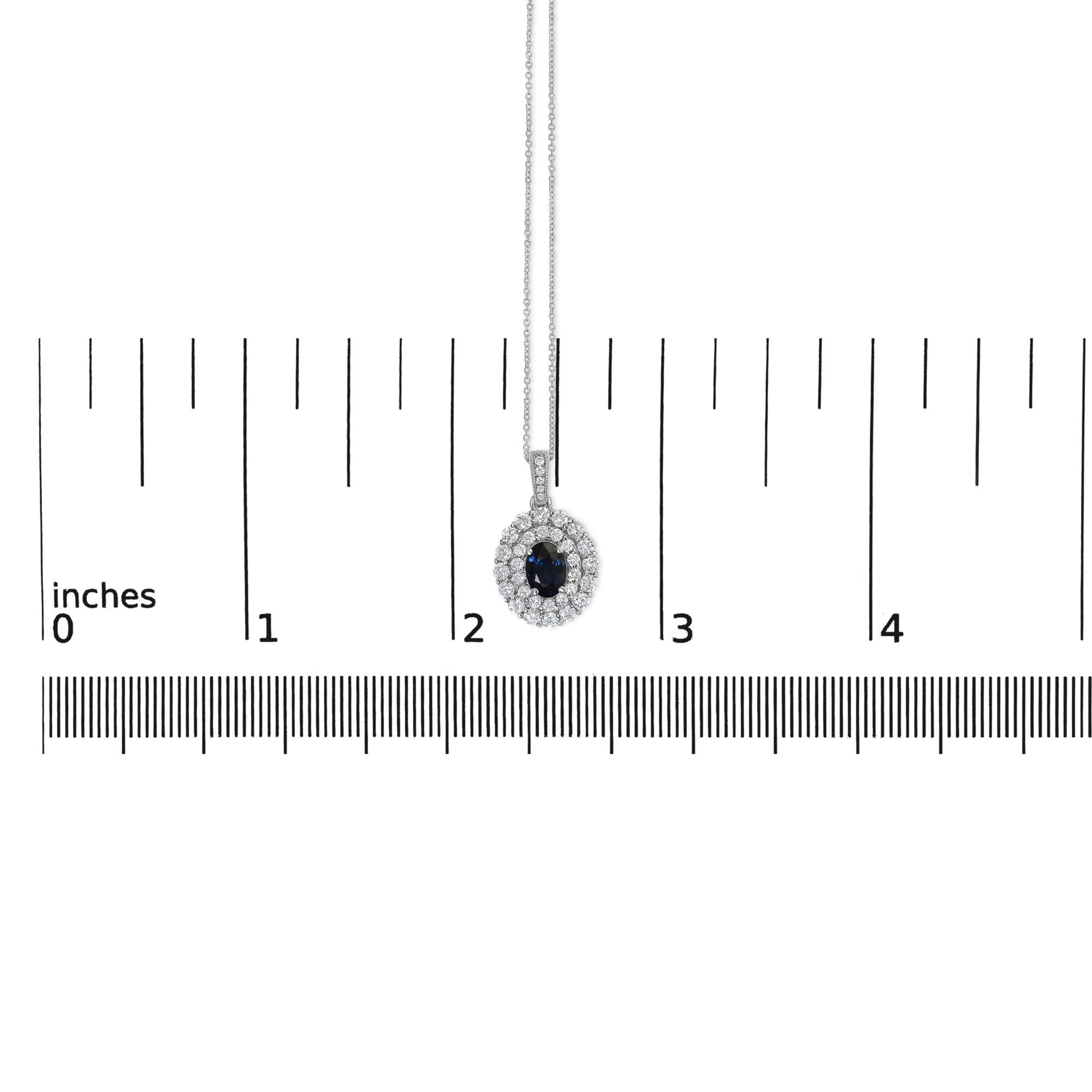 White metal necklace with oval blue gemstone pendant surrounded by two rows of round white gemstones in prong settings, shown hanging centered on a ruler scale from a front angle.