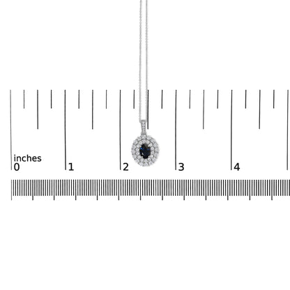 White metal necklace with oval blue gemstone pendant surrounded by two rows of round white gemstones in prong settings, shown hanging centered on a ruler scale from a front angle.