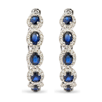 Close-up front view of white metal earrings featuring oval blue gemstones surrounded by small round white gemstones in prong settings.