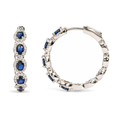 Close-up front and side view of white metal hoop earrings set with oval blue gemstones surrounded by small round white gemstones in prong settings.