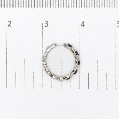 Close-up top view of a white metal hoop earring with blue oval gemstones and small white round gemstones in a prong setting, shown on a measurement scale.