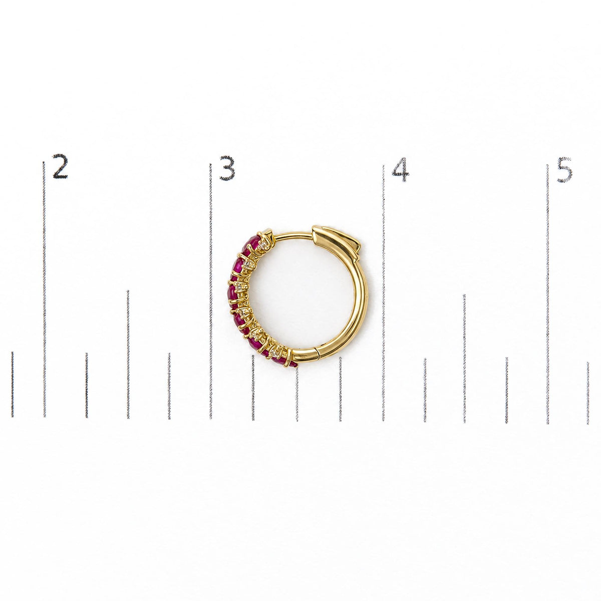 Close-up front angle of a yellow metal hoop earring set on a scale, featuring oval red gemstones and round white gemstones in prong settings along half its outer edge.