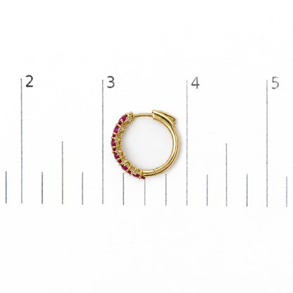 Close-up front angle of a yellow metal hoop earring set on a scale, featuring oval red gemstones and round white gemstones in prong settings along half its outer edge.