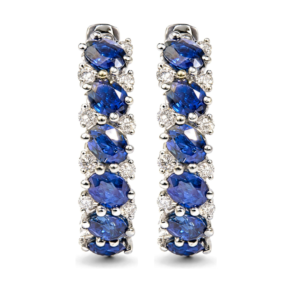 Close-up front view of a pair of white metal earrings featuring oval-shaped blue gemstones and multiple round white gemstones in prong settings.