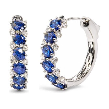Close-up front angle of white metal hoop earrings featuring oval blue gemstones surrounded by round white gemstones in prong settings.
