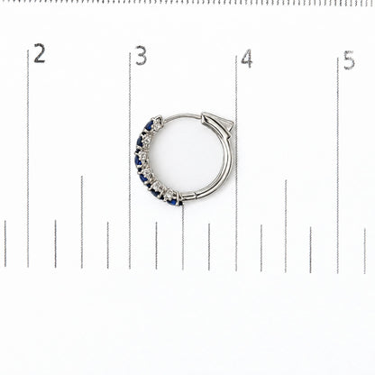 Close-up top view of a white hoop earring displayed on a scale, featuring alternating prong-set oval blue gemstones and round white gemstones along one side.