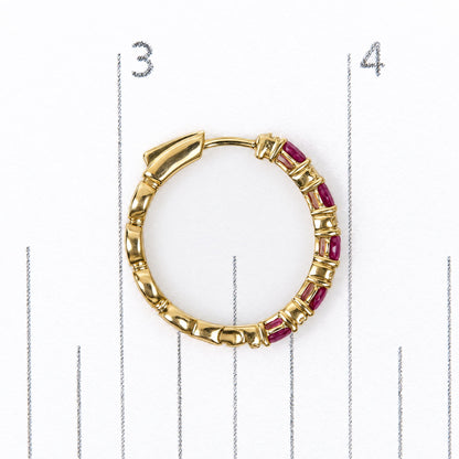 Close-up, top-down view of a yellow metal earring set on a measurement scale. The hoop earring features oval-shaped red gemstones and sections of smooth yellow metal.