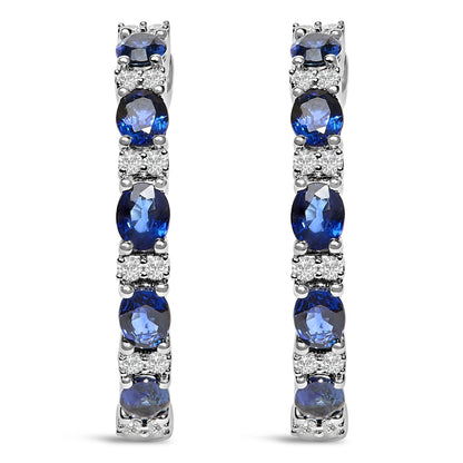 Front view of pair of white metal earrings featuring alternating oval blue gemstones and round white gemstones in shared prong and 4-prong settings.
