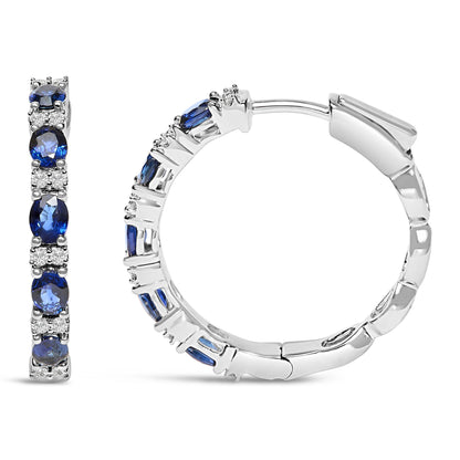 Pair of white metal hoop earrings with alternating round white gemstones and oval blue gemstones in prong settings, shown from front and side angles on a white background.