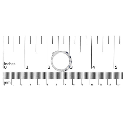 Close-up front view of a white metal hoop earring with alternating small white round gemstones and blue oval gemstones set in prongs, placed on a ruler for size reference.