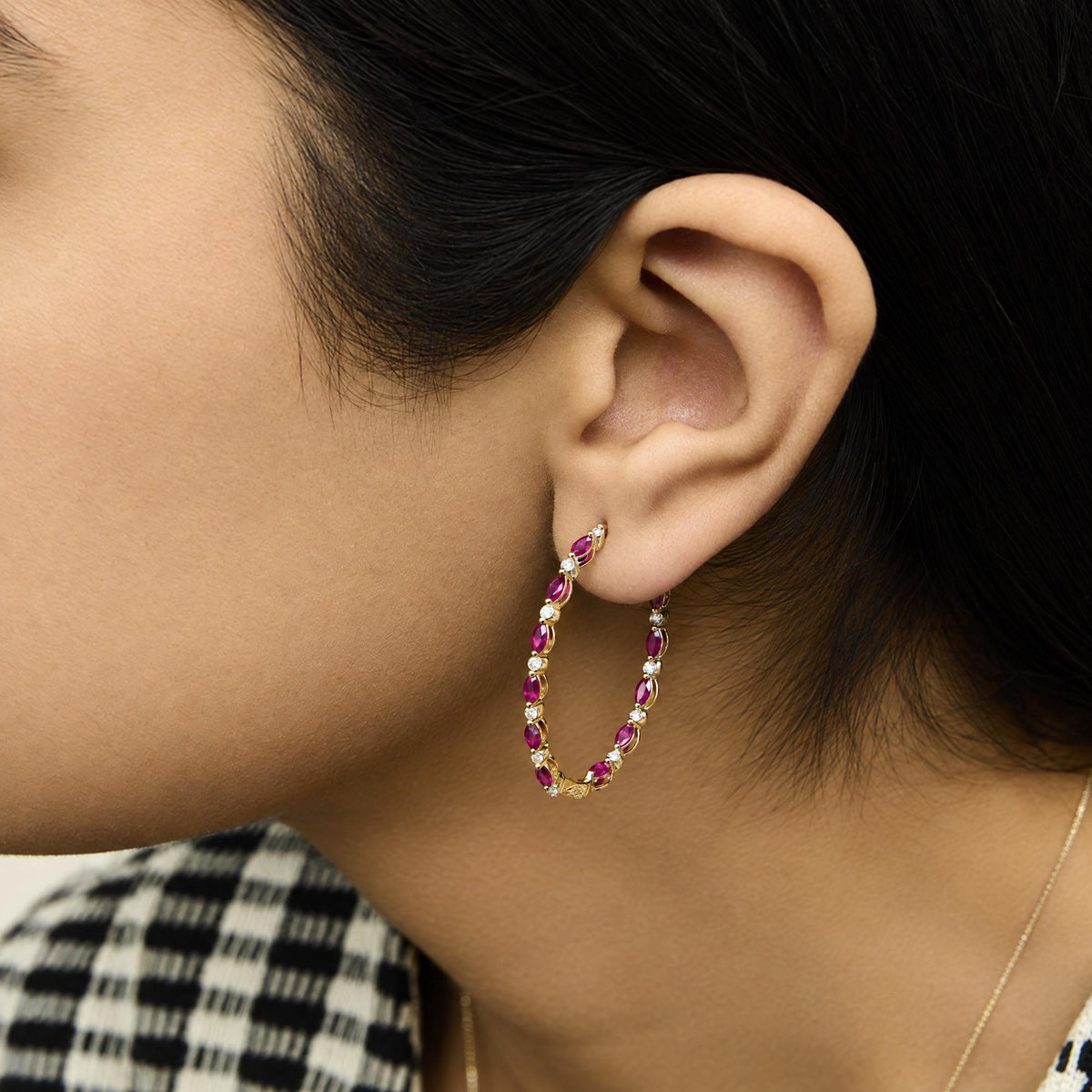 Close-up side view of a model wearing yellow metal hoop earrings featuring alternating marquise-shaped red gemstones and round white gemstones in prong settings.