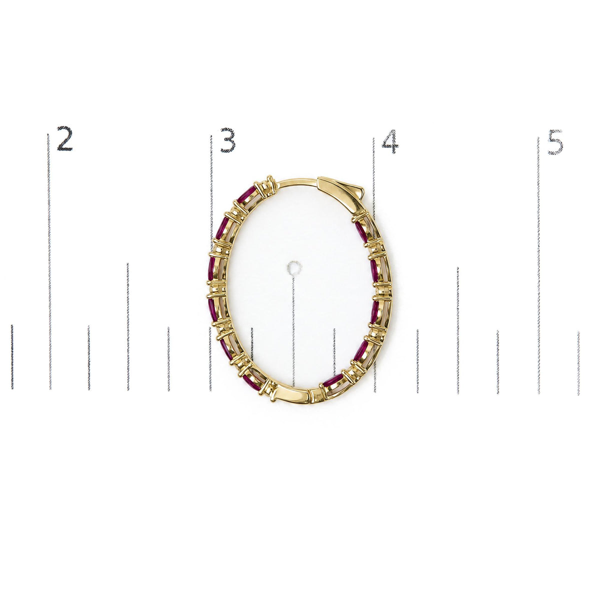 Close-up overhead view of a yellow metal hoop earring with alternating red marquise-shaped gemstones and white round gemstones in prong settings, shown on a scale.