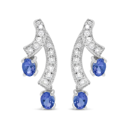 Pair of white metal earrings with curved design, prong-set with round white gemstones along the curves and blue oval gemstones at the ends, shown in a front-facing view.