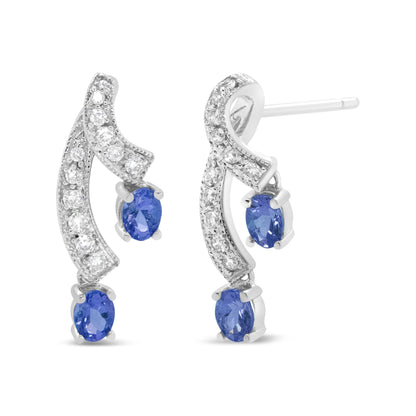 Pair of white metal earrings shown from a front and slight side angle, featuring curved rows of small round white gemstones and two oval blue gemstones on each earring in prong settings.