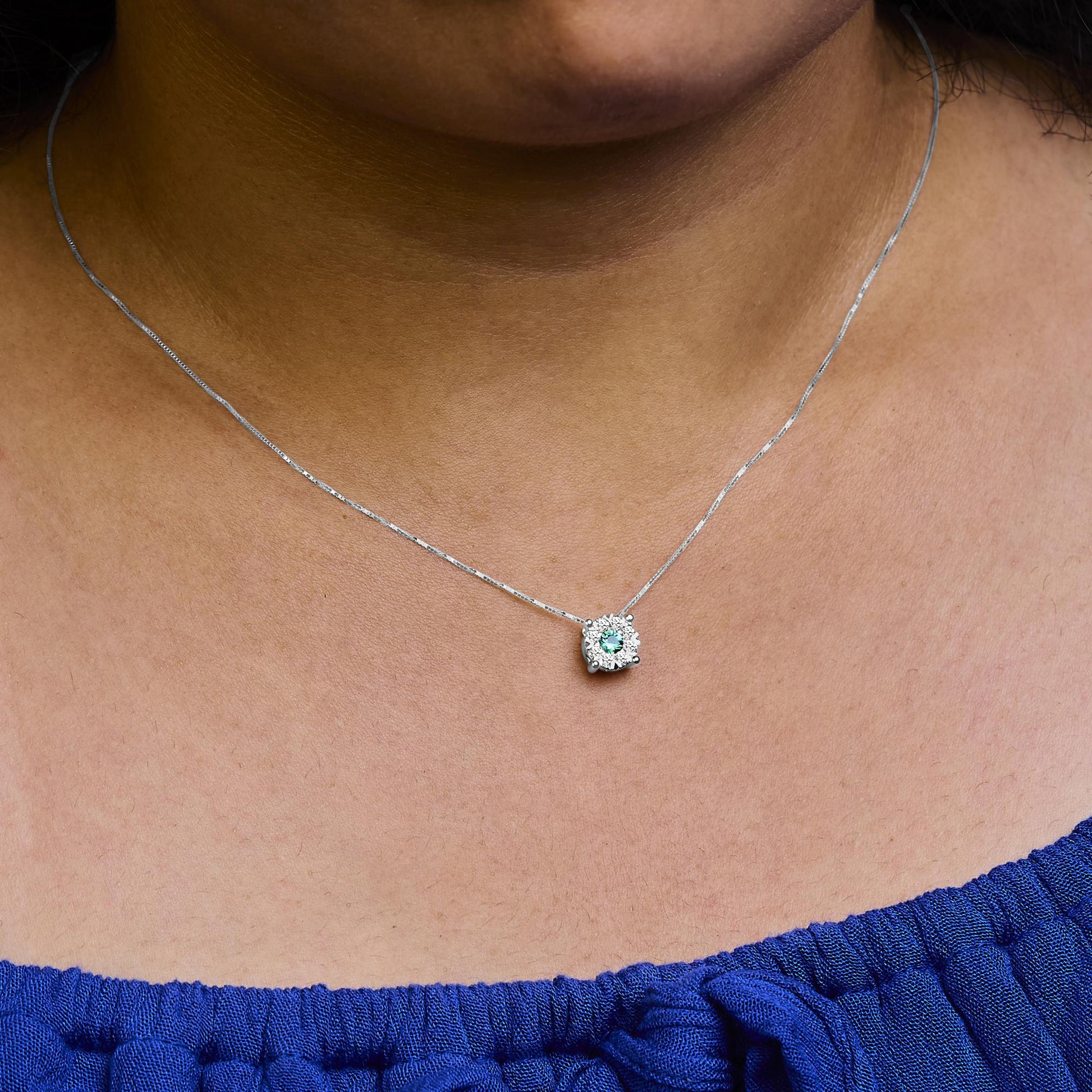 Close-up front view of a white metal necklace on a model, featuring a round green gemstone surrounded by multiple small round white gemstones in a pave setting.