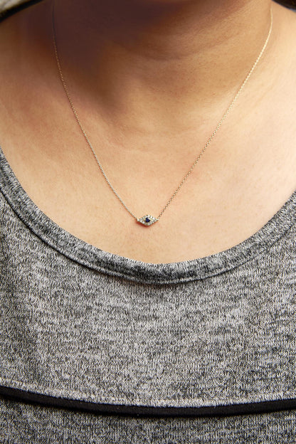 Close-up front view of a yellow metal necklace on a model, featuring a central round blue gemstone surrounded by small white round gemstones in a pave setting.