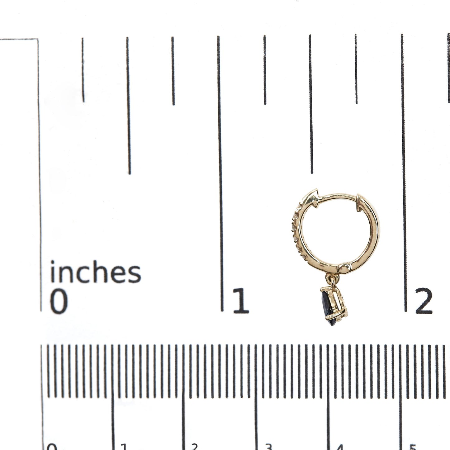 Close-up front angle of a yellow metal hoop earring with small white gemstones along the outer edge and a dangling pear-shaped blue gemstone, shown on a ruler for size reference.